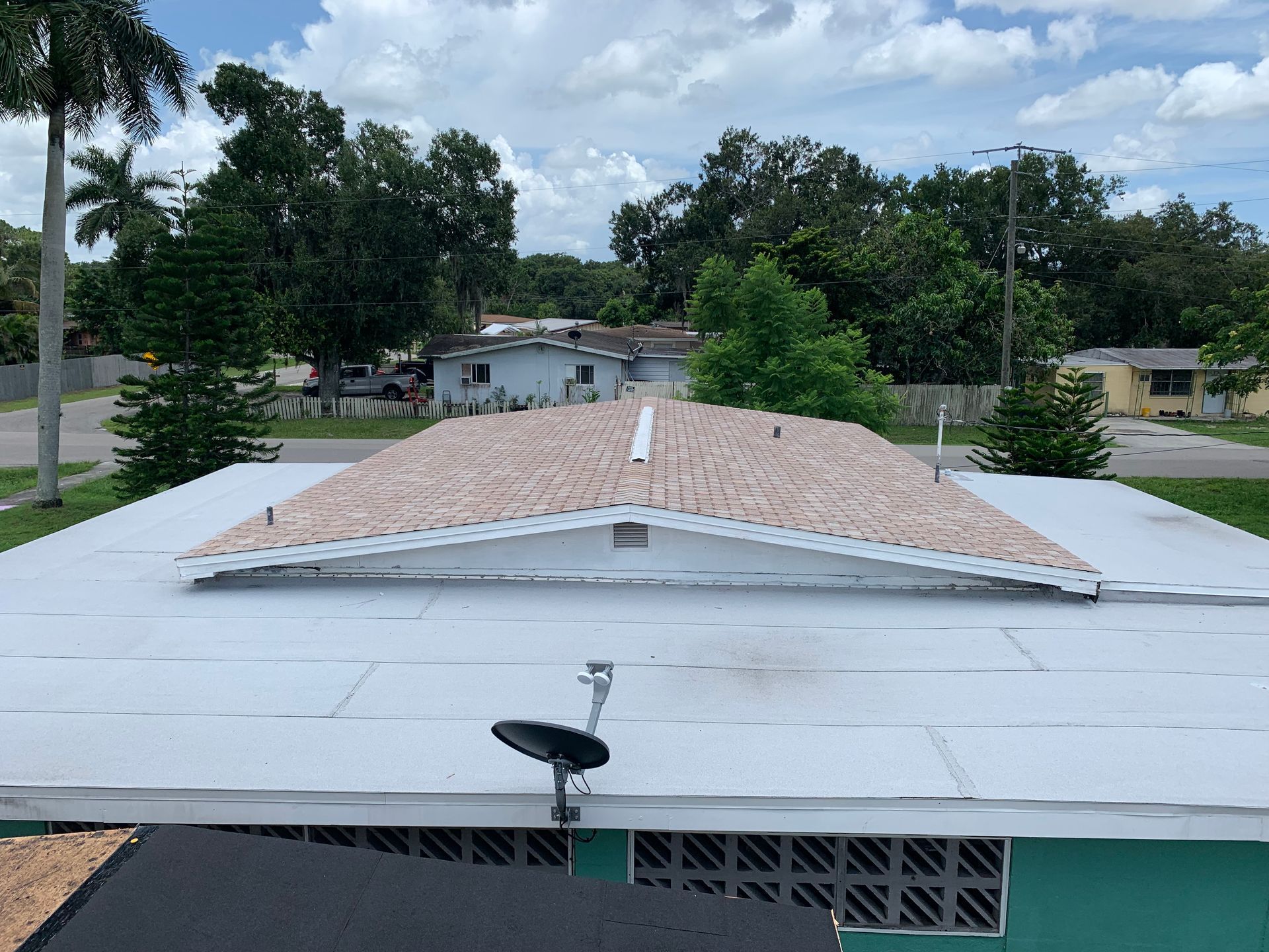 Rooftop with white flat roof and small tiled section, overlooking trees and houses under cloudy sky