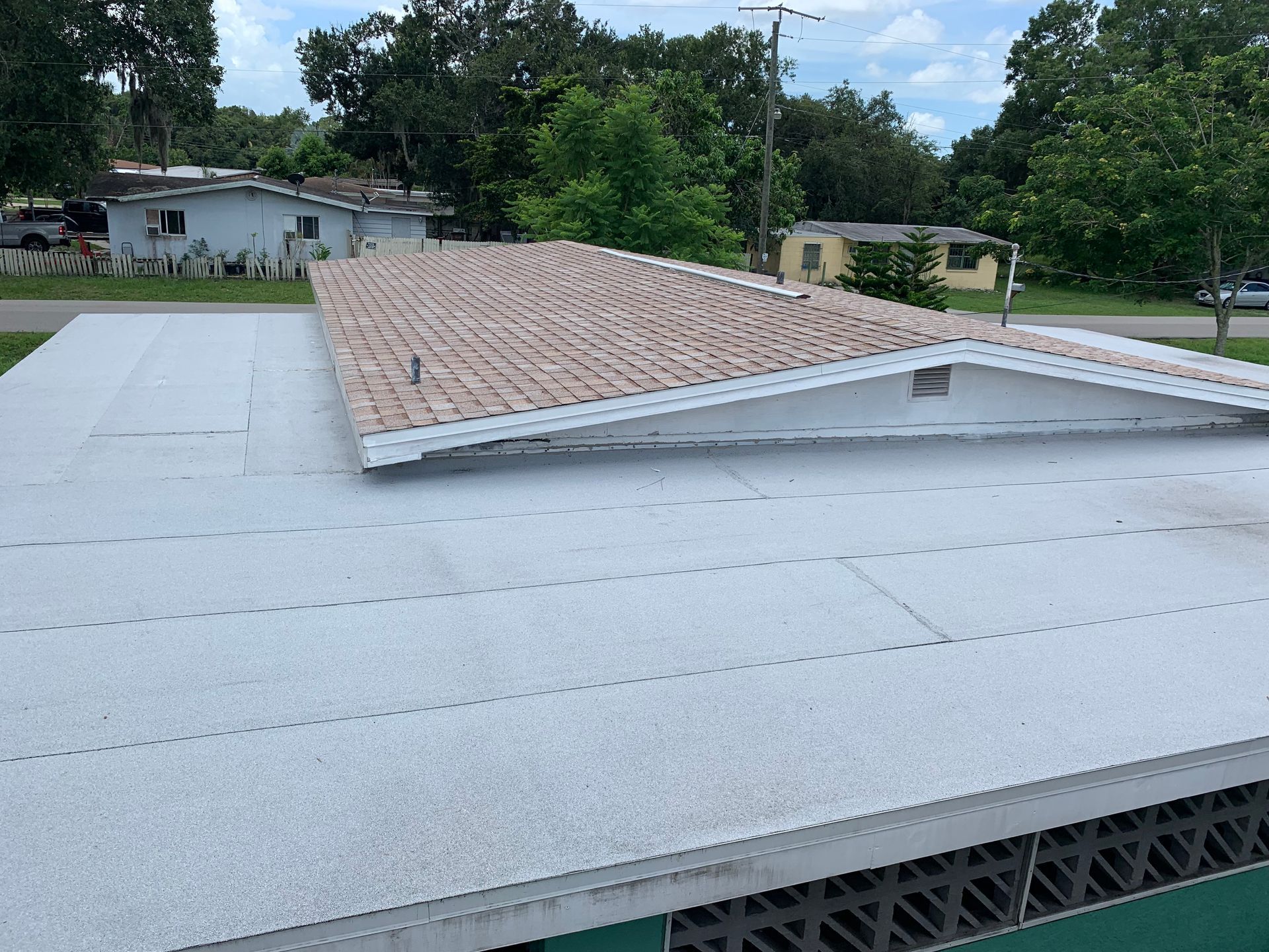 White roof with a tan shingled section in a suburban neighborhood, seen from above