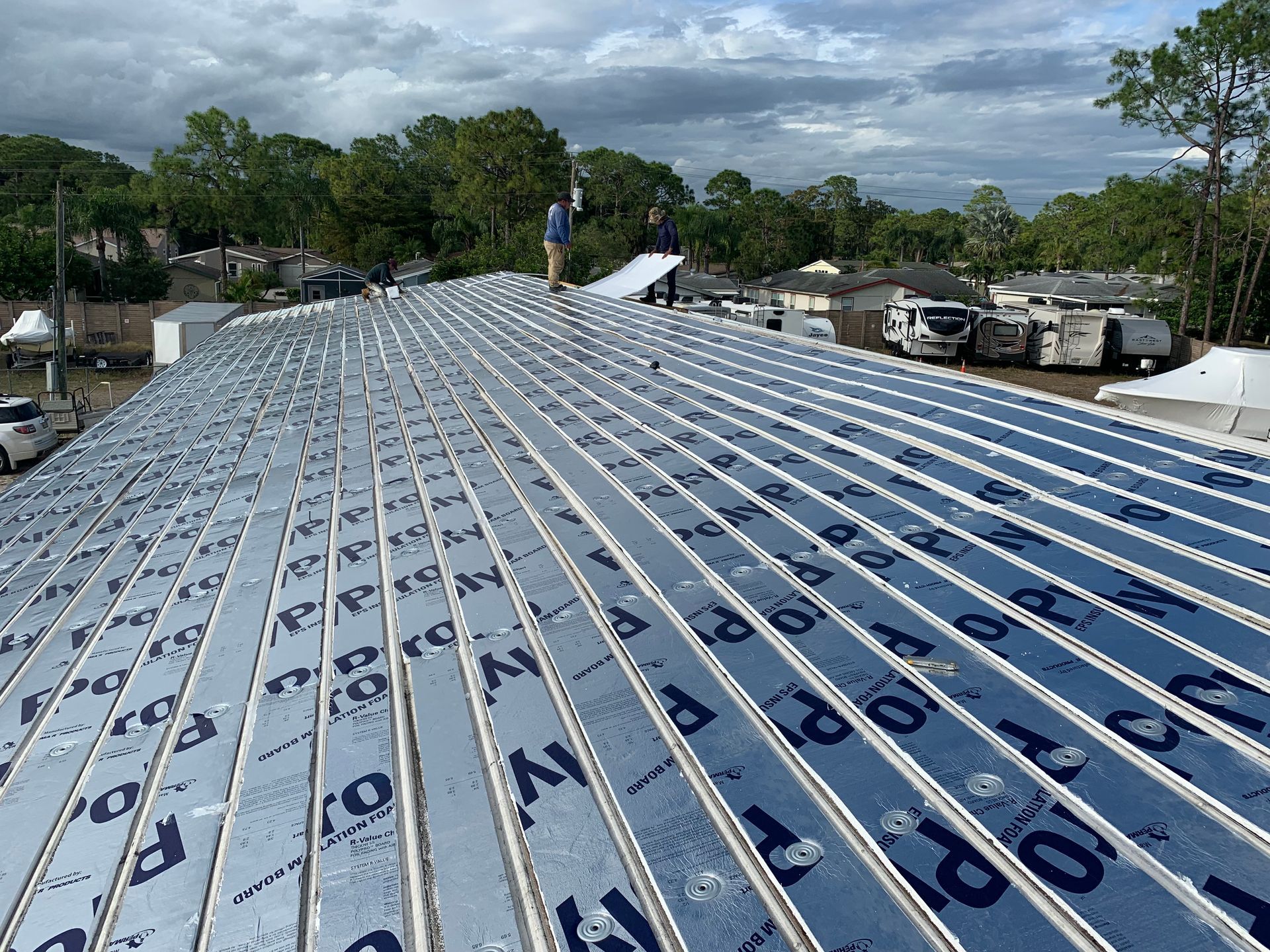 Roof under construction with blue underlayment and metal battens, with trucks and cloudy sky in the background