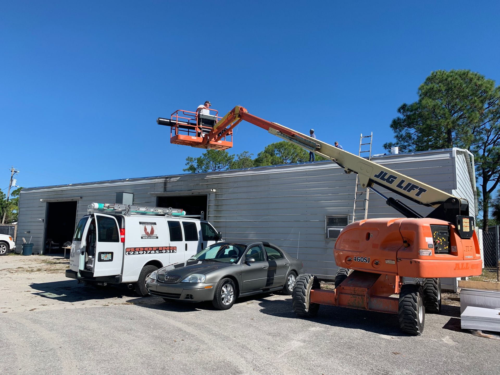 Tow truck hoisting equipment above a white van and damaged car outside a building under construction.