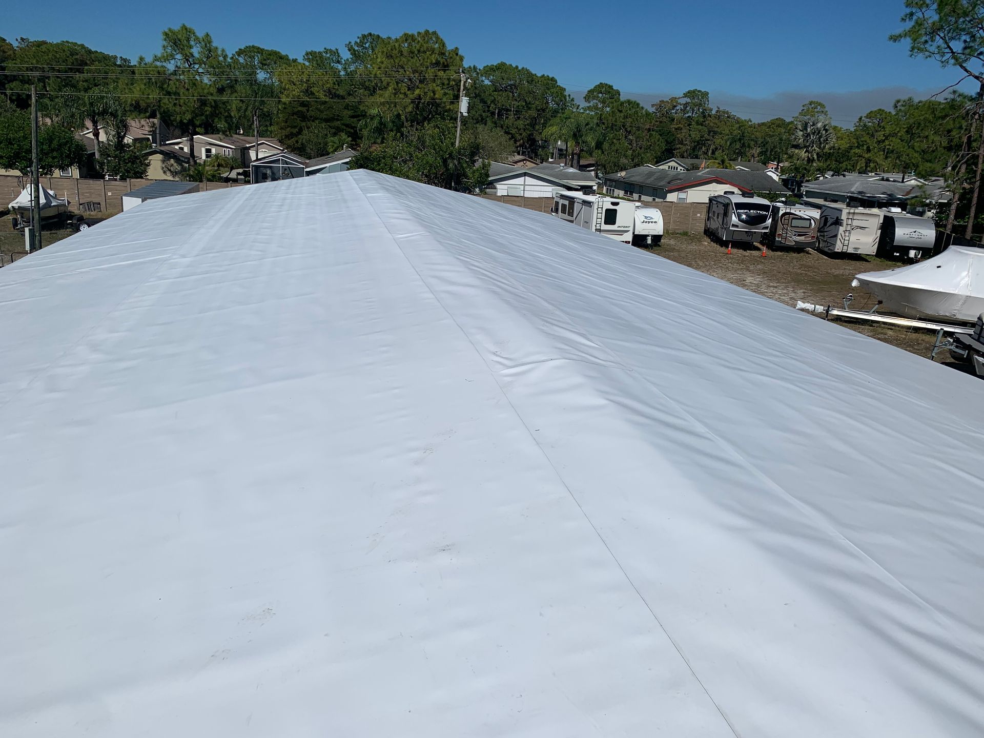 White tarp-covered roof in a suburban neighborhood under a clear blue sky