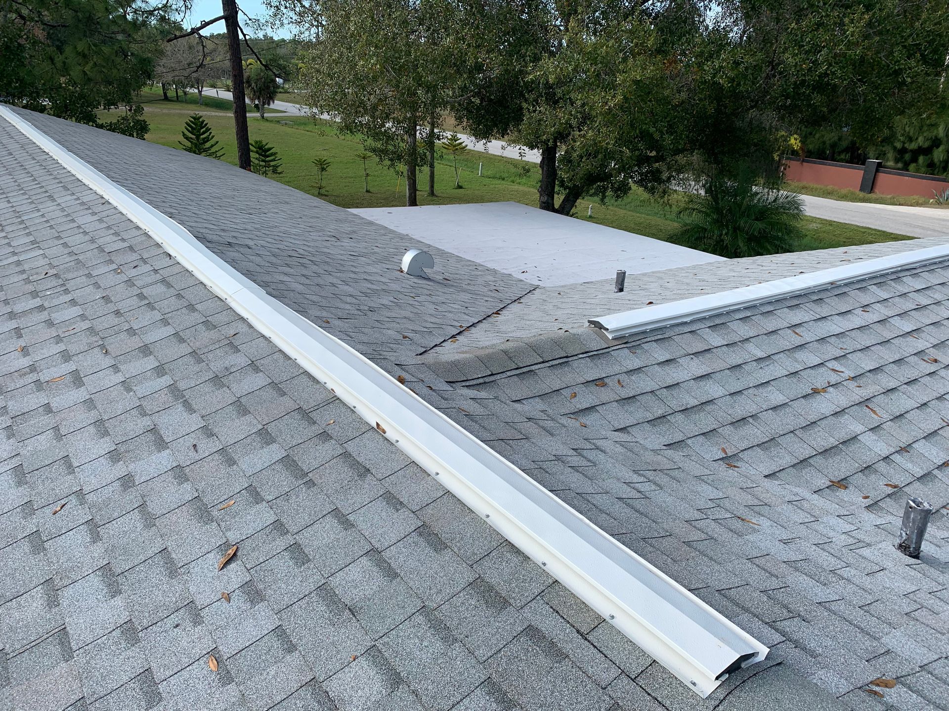 Gray shingled roof with a white gutter and a small skylight, overlooking trees and a walkway