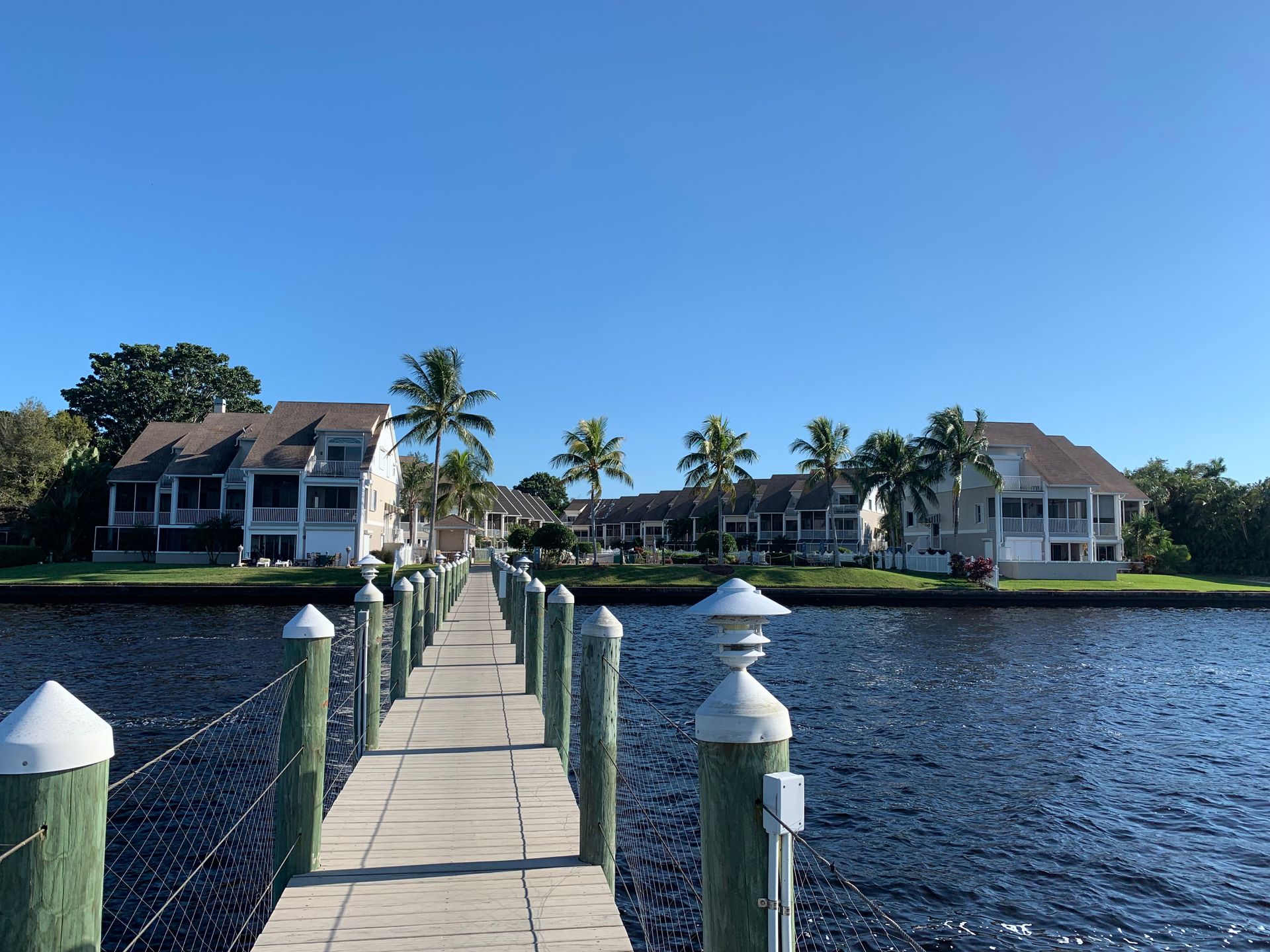 Wooden dock leading to waterfront homes with palm trees under a clear blue sky