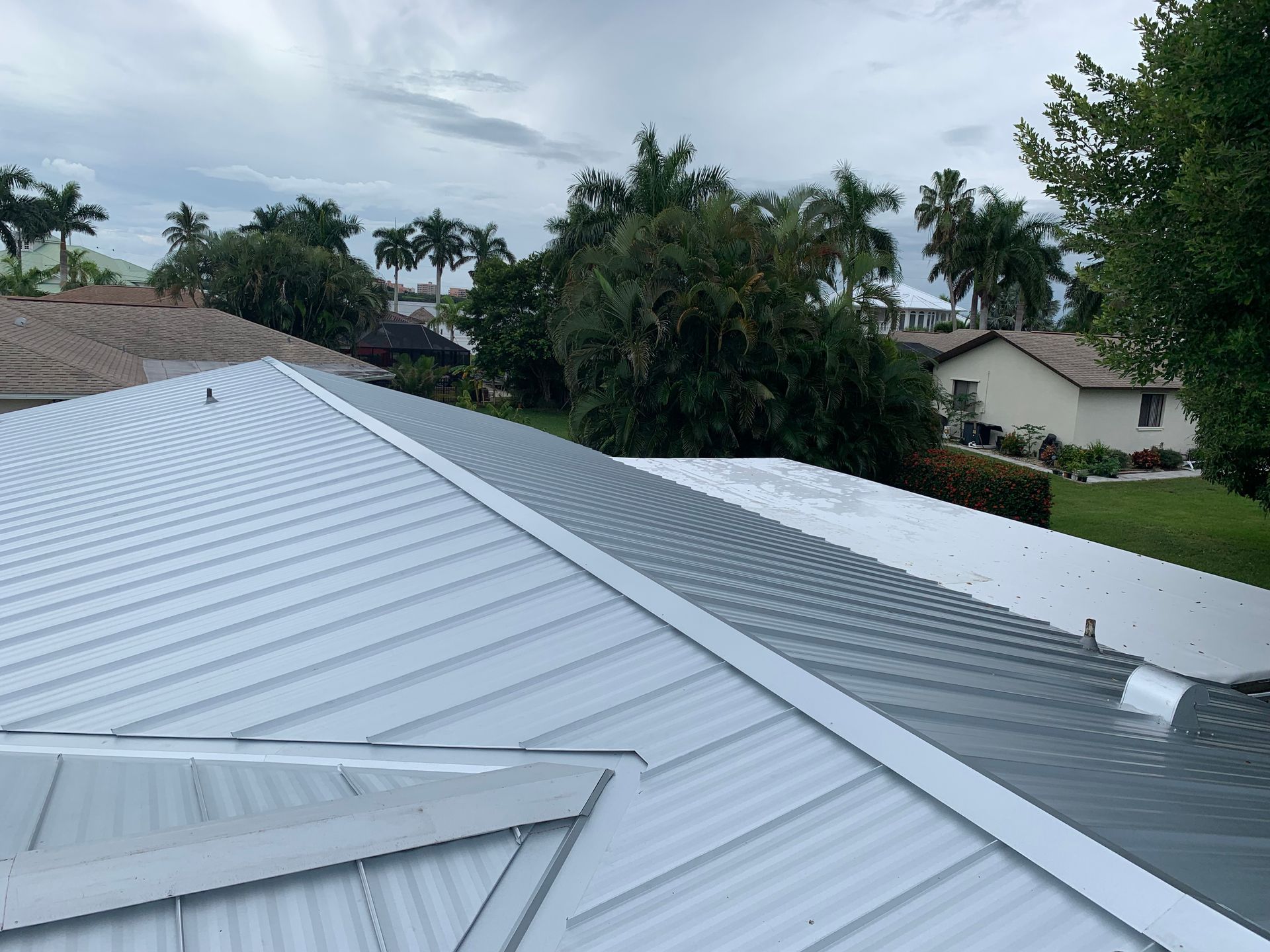 White and gray metal roof on a house with trees and cloudy sky in the background
