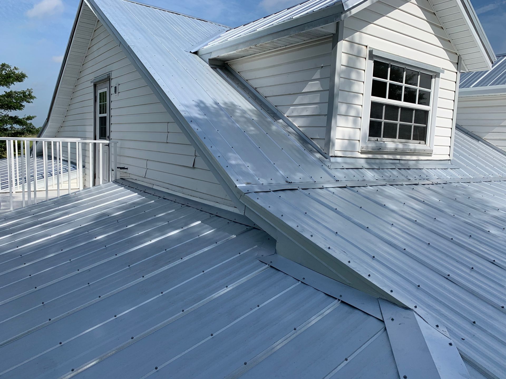 Snow-covered metal roof with dormer windows and white railing under bright sunlight