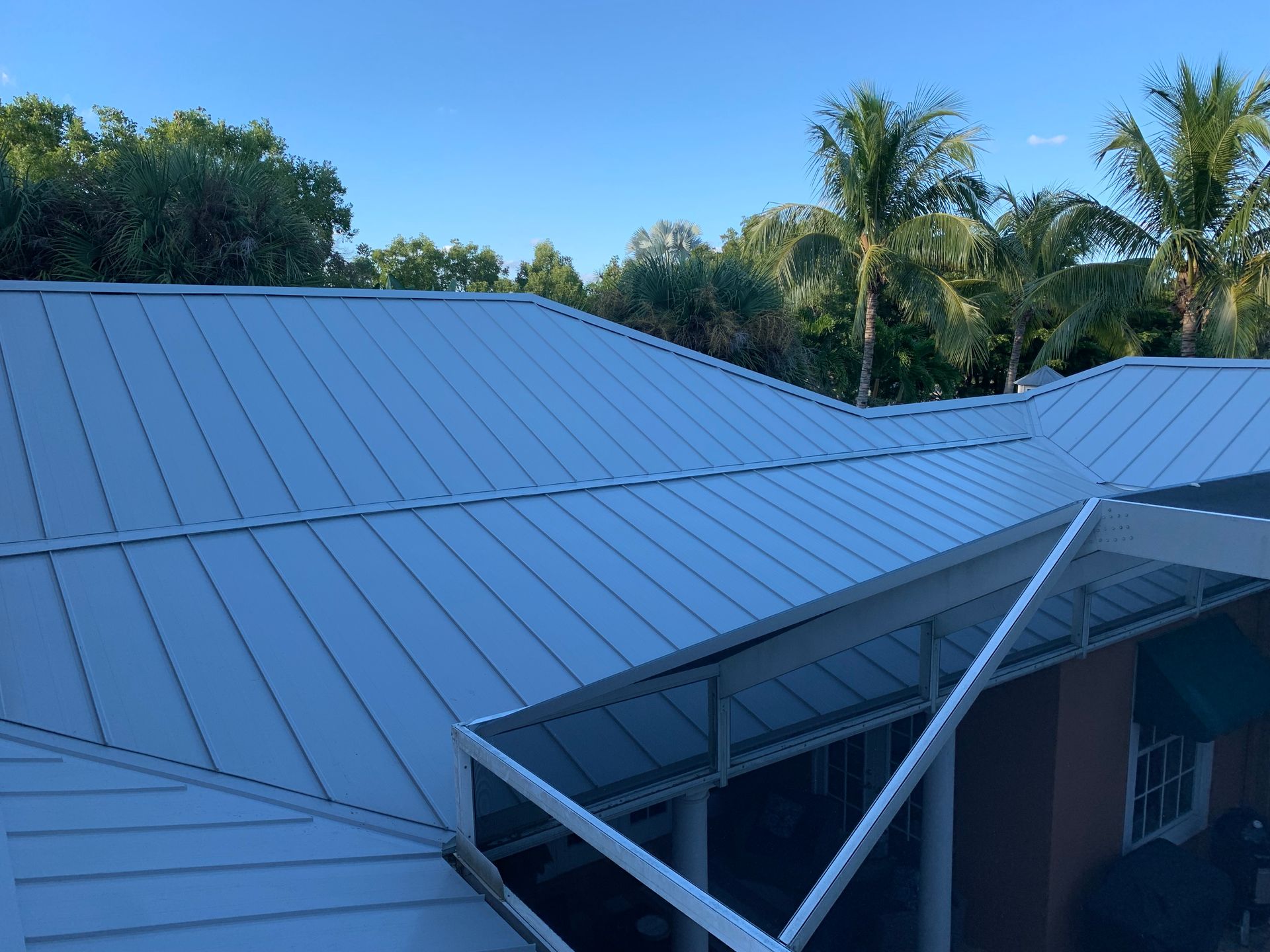 Blue metal roof with a damaged section and supporting beams against palm trees and sky
