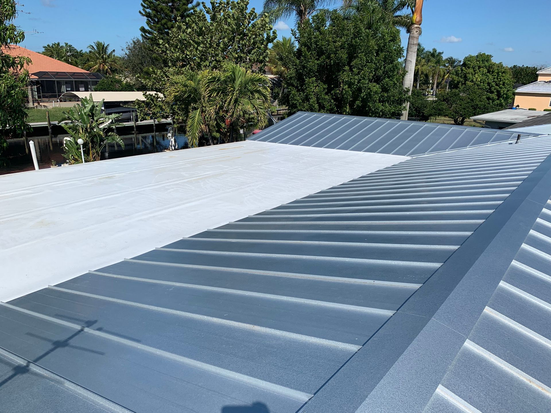 White and gray corrugated metal roof in bright sunlight, with trees and houses in the background