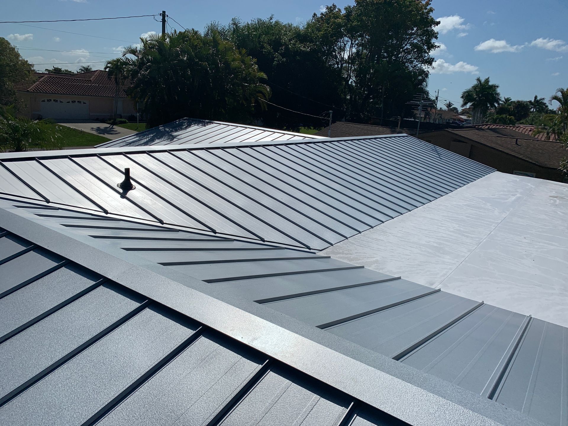 Gray metal roof with standing seams and skylights under a sunny sky, viewed from above
