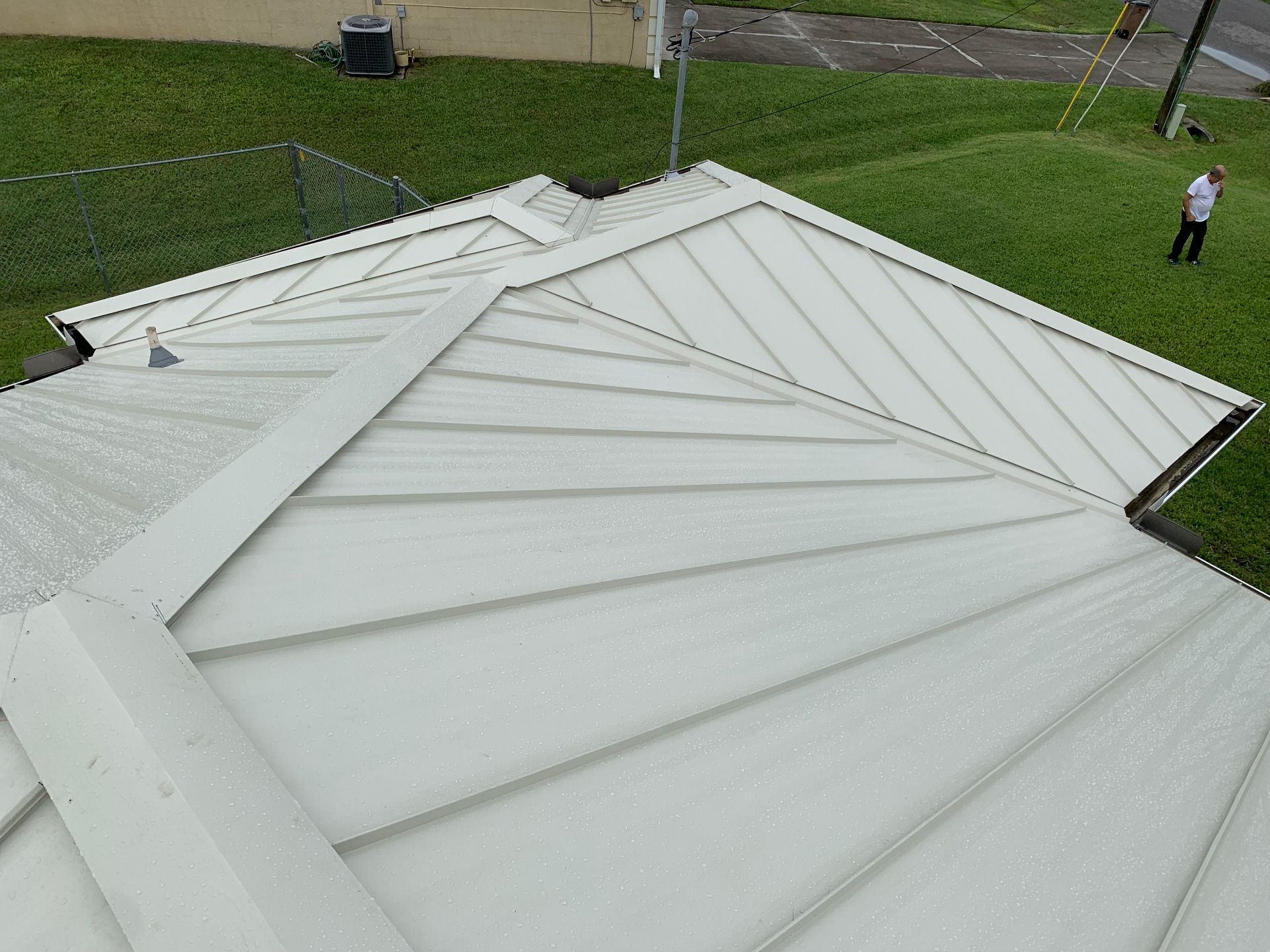 White metal roof viewed from above, with a person standing on the lawn nearby.