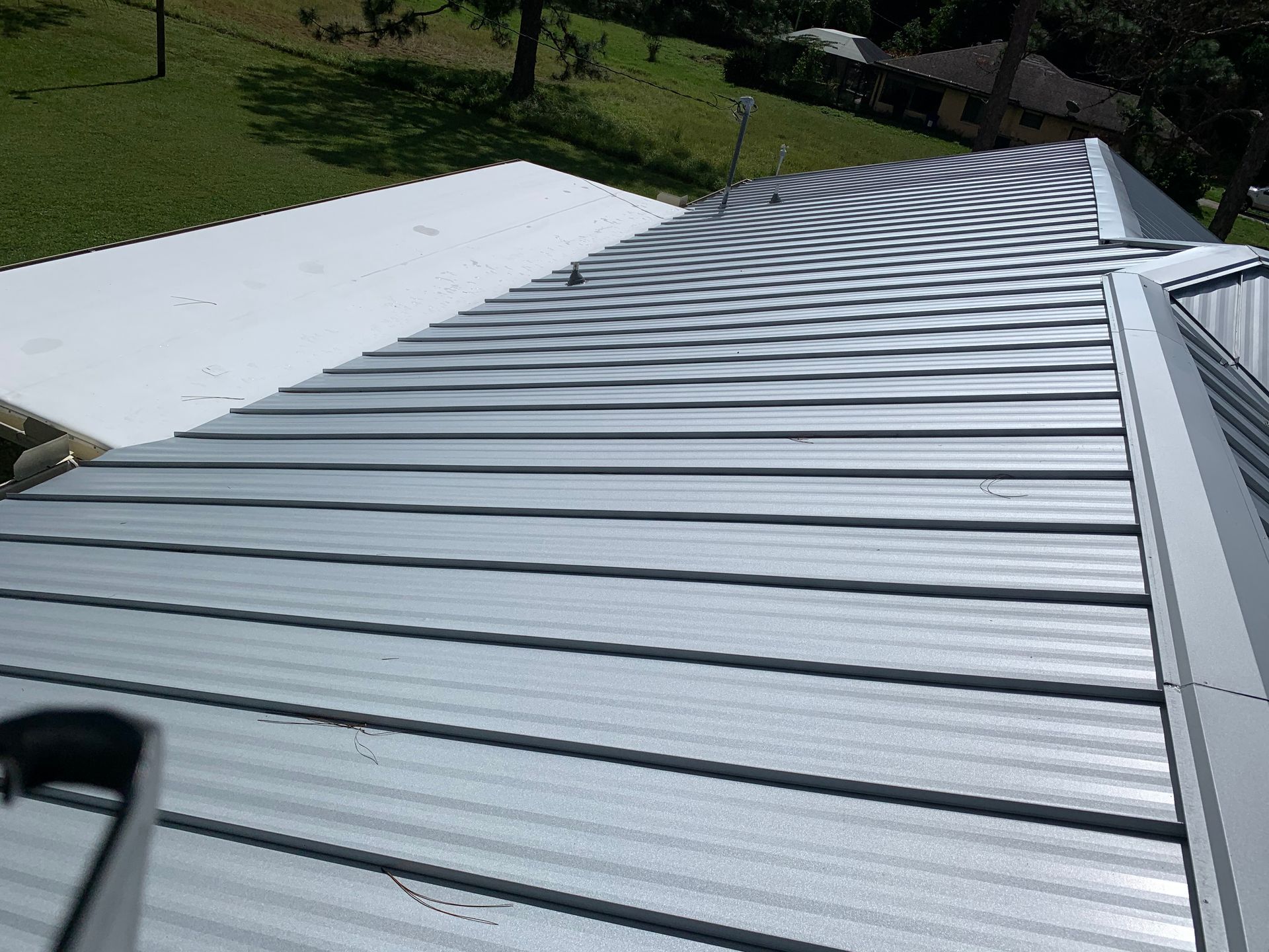White corrugated metal roof sloping beside a green grassy yard and trees