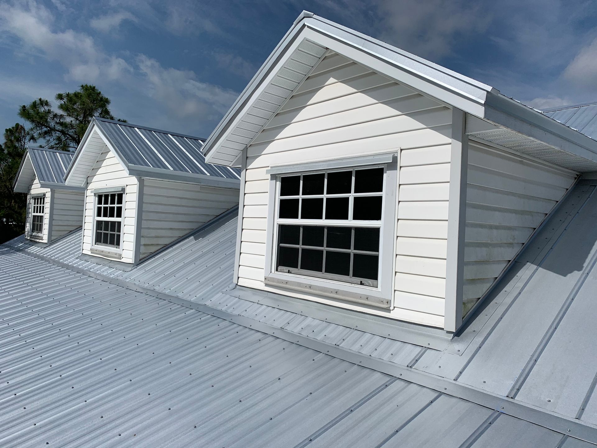 White metal roof with two dormer windows under a clear blue sky.