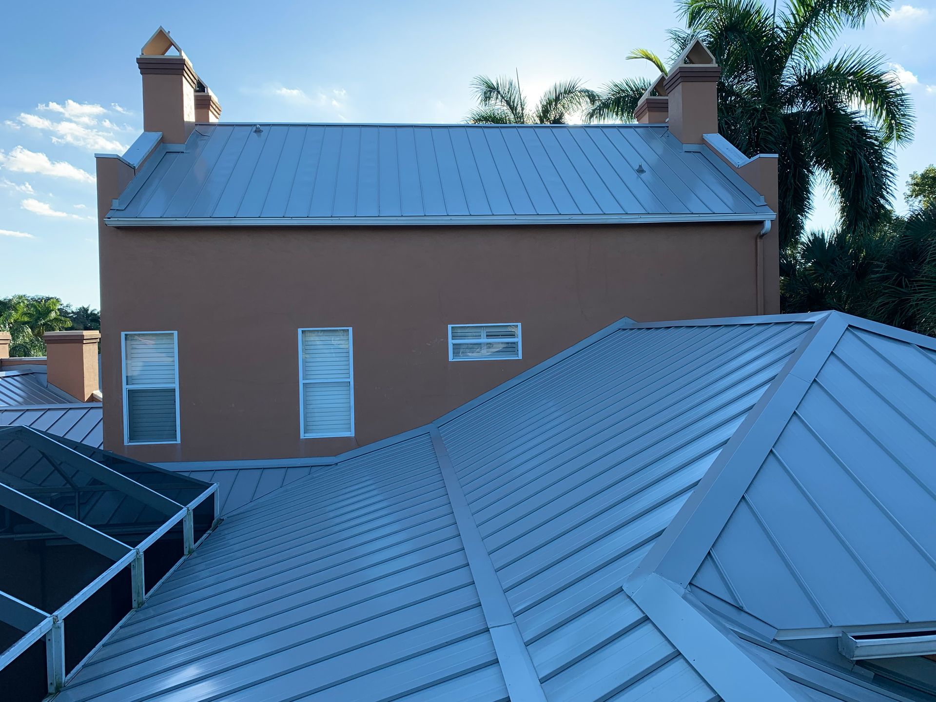 Rooftops with blue metal panels and a brown stucco building under a clear sky