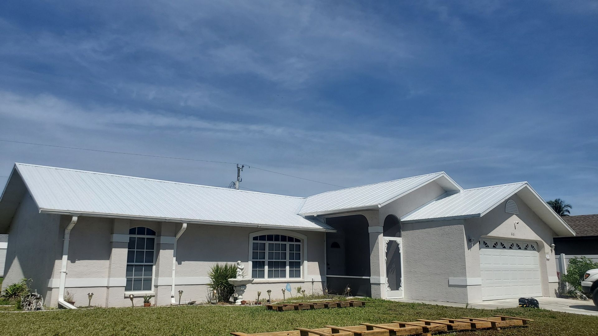 Single-story white house with a metal roof under a clear blue sky, front lawn in sunlight