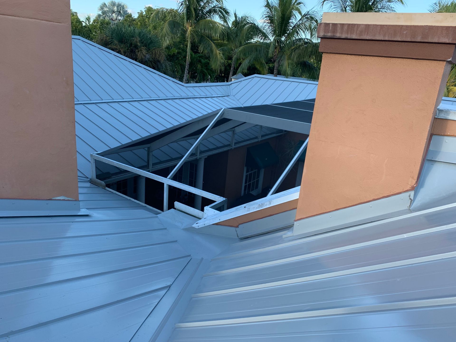 Metal roof with skylight opening, seen between two orange chimney structures and trees in the background