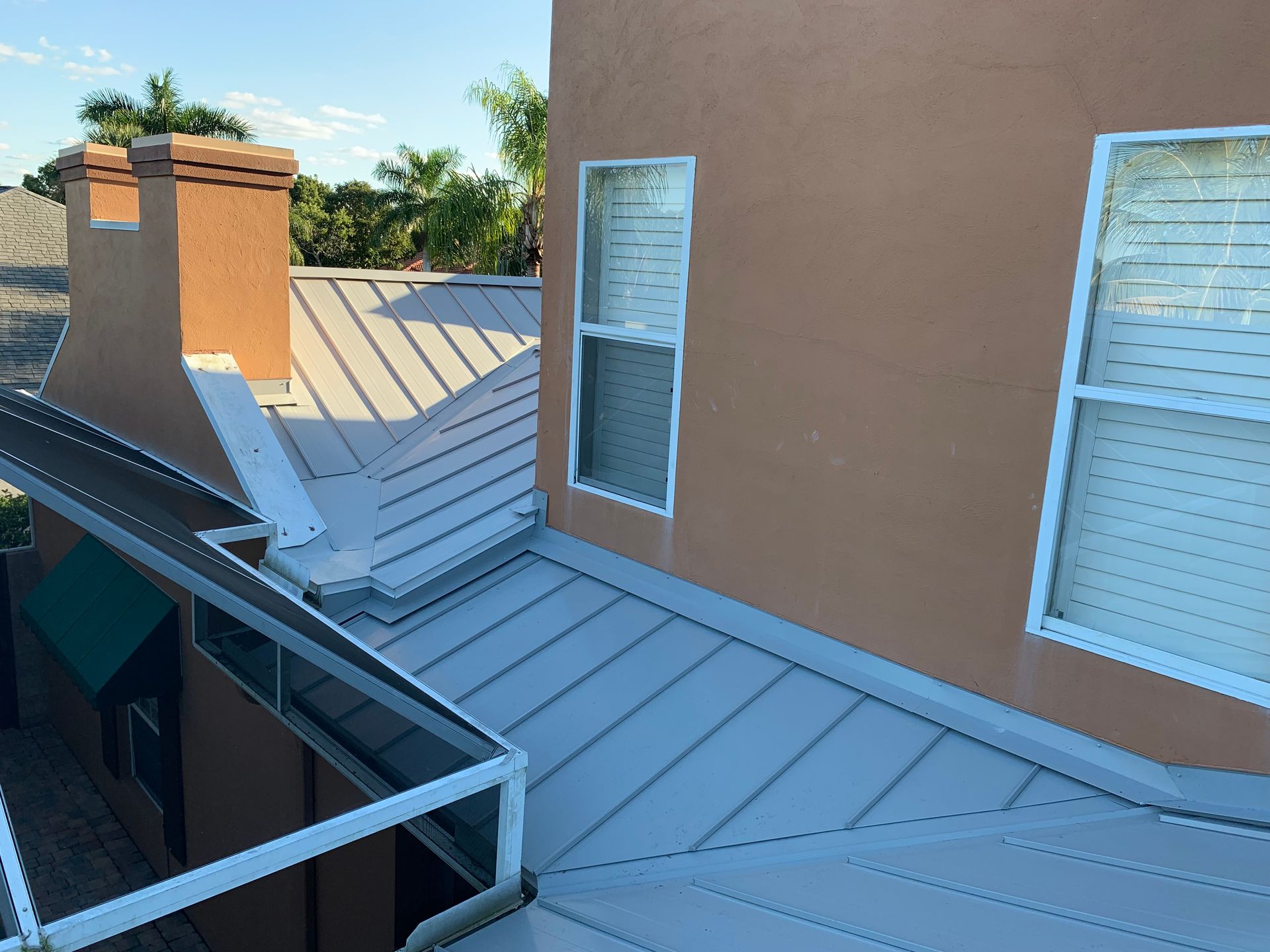 Rooftop patio with gray metal roofing, tan stucco wall, and two windows under bright daylight