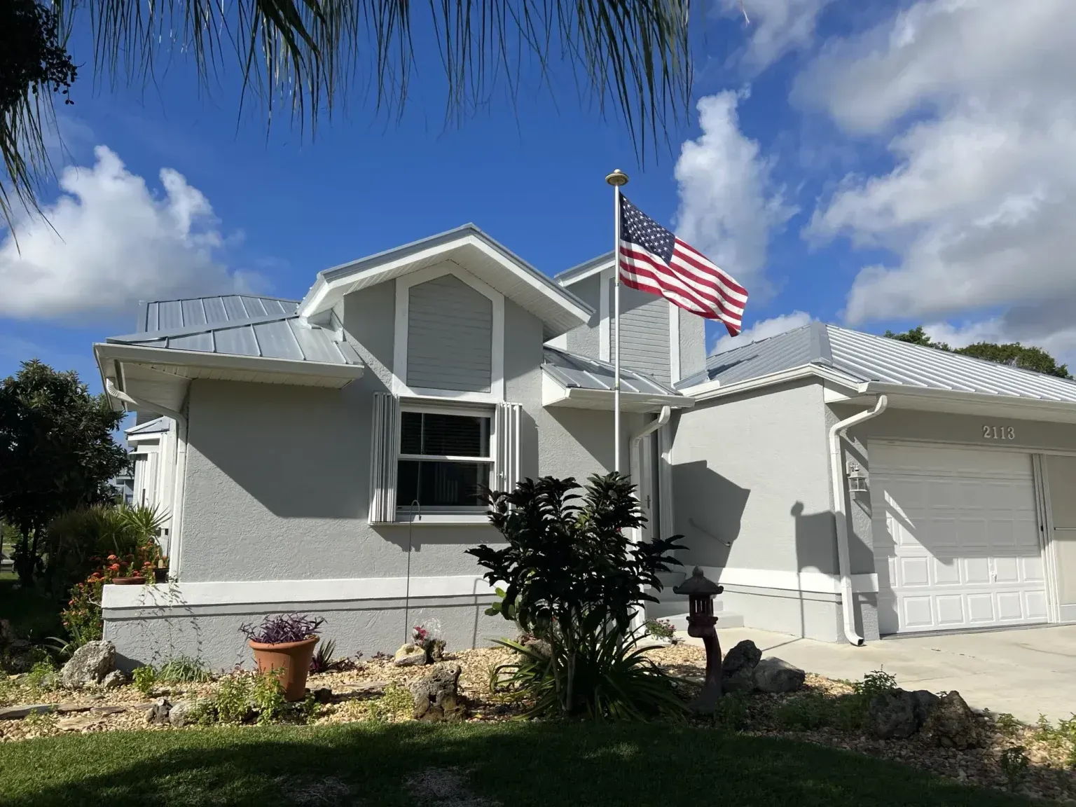 White suburban house with a U.S. flag flying in front and a two-car garage under a blue sky