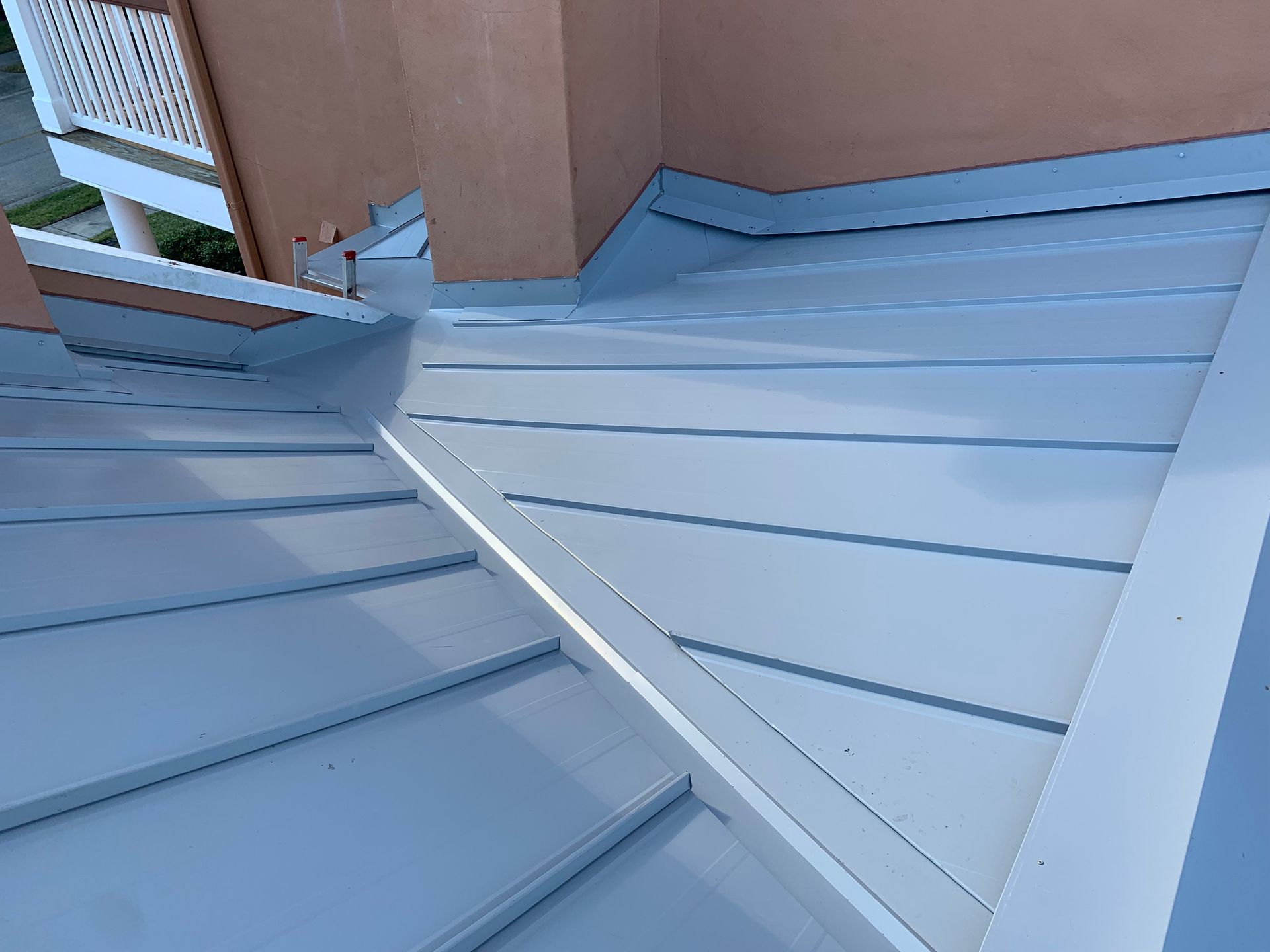 Gray metal roof with standing seams and a triangular section beside a building wall