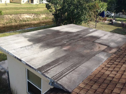 Damaged flat roof with a large patch of rolled roofing beside brown shingles.