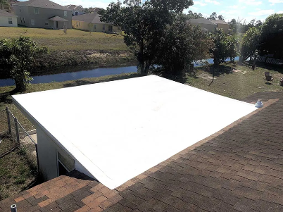 White canopy or tarp stretched over a backyard patio beside a brick roof and grassy yard
