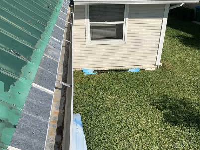 Roof edge beside a beige house and green lawn, with blue vent covers near the wall.