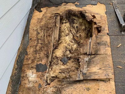 Rotted wooden deck board with a large hole and exposed decayed wood near a wall