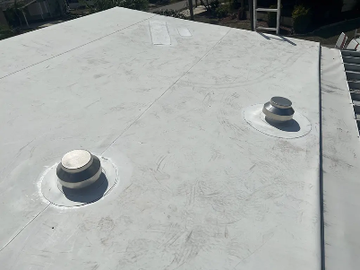 Flat white rooftop with two vent pipes and a small skylight near the edge