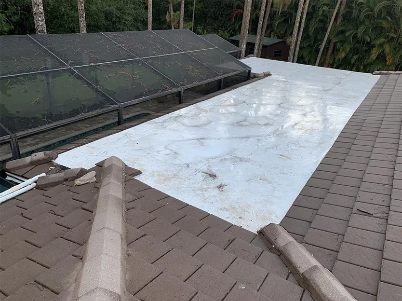 Roof with white tarp covering a section beside brown shingles and a dark skylight roofline