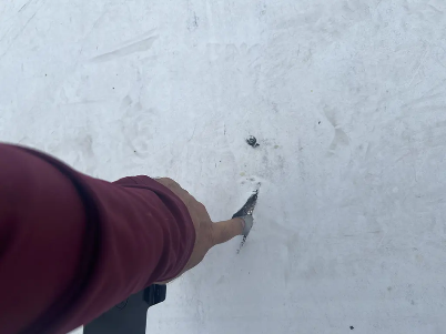 Person in maroon sleeve reaching toward a small hole in a white wall or ceiling surface.