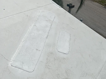 White rooftop with two long rectangular patches or skylights near a dark edge and water in the background