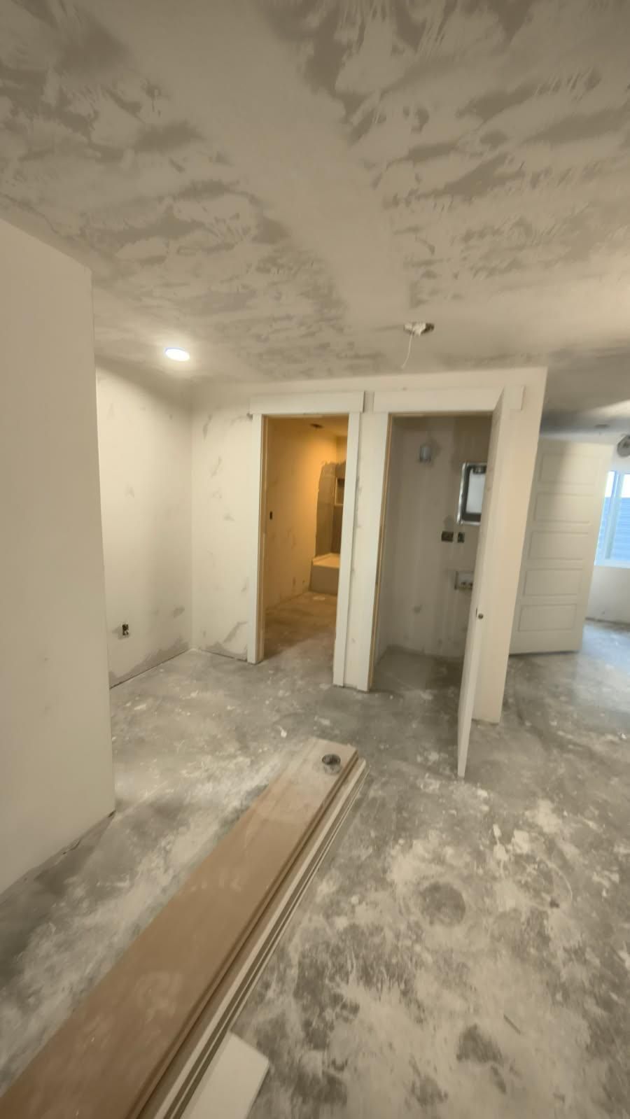 Partially renovated room with unfinished walls, exposed ceiling, and a doorway to a lit hall