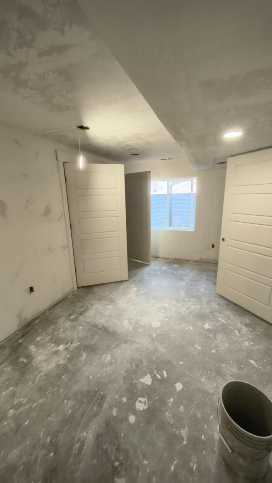 Unfinished room with white doors, bare walls, and a window letting in daylight