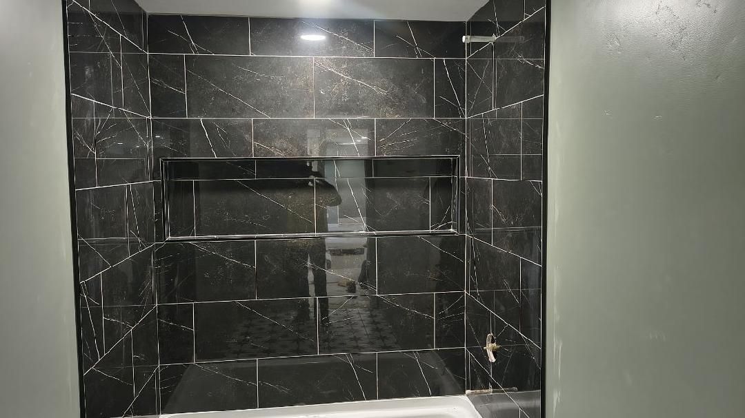 Black marble shower niche with built-in shelves under a bright ceiling light.
