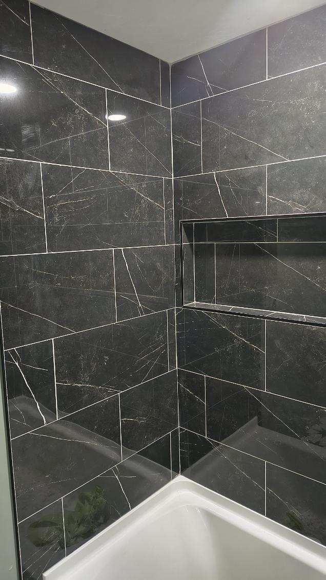 Dark tiled shower corner with built-in shelf and white tub edge