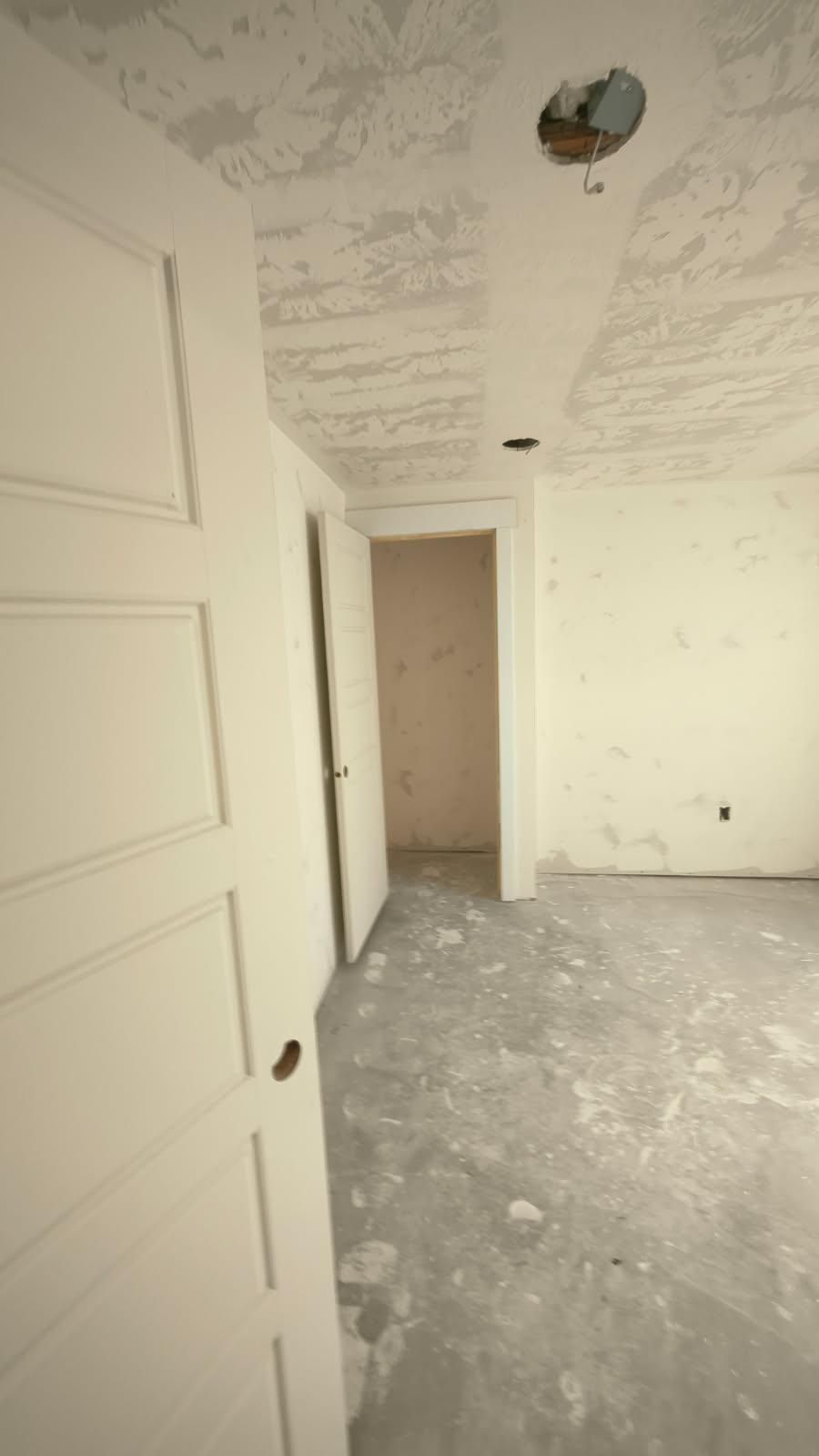 Empty unfinished room with white walls, gray floor, and open doorways, under renovation