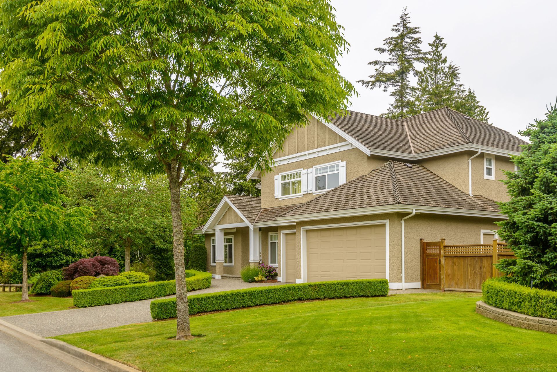 Suburban two-story beige house with a green lawn and large trees in front