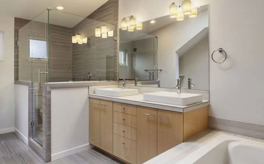 Modern bathroom with wood vanity, dual sinks, glass shower, and gray tile.