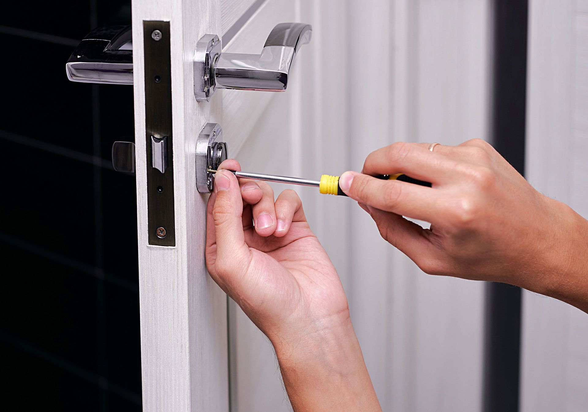 Person using a screwdriver to install a lock on a white door.
