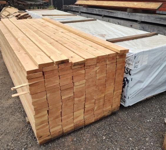 A stack of wood is wrapped in plastic and sitting on the ground.