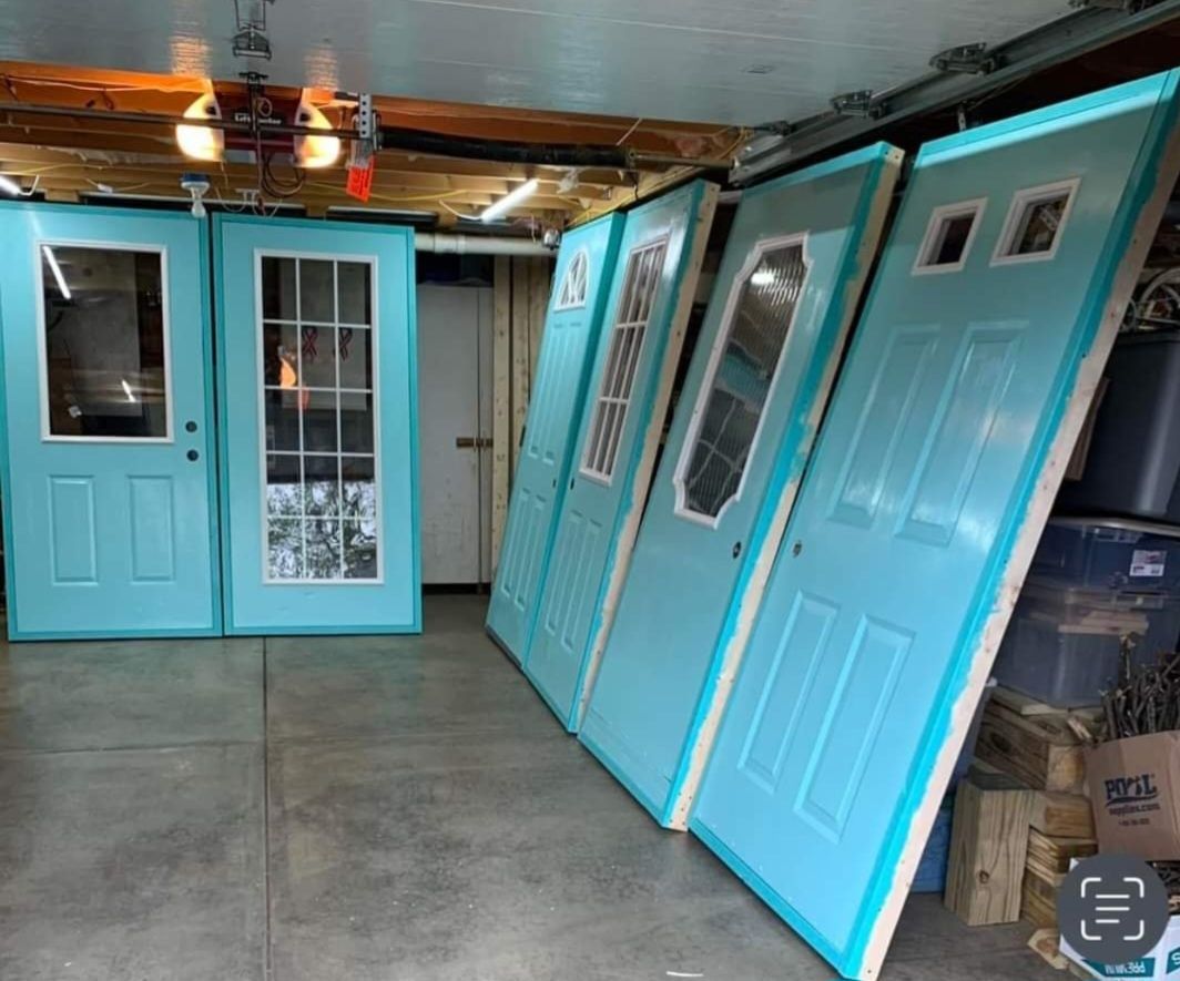 Six light-blue doors with various glass window designs standing upright in a garage