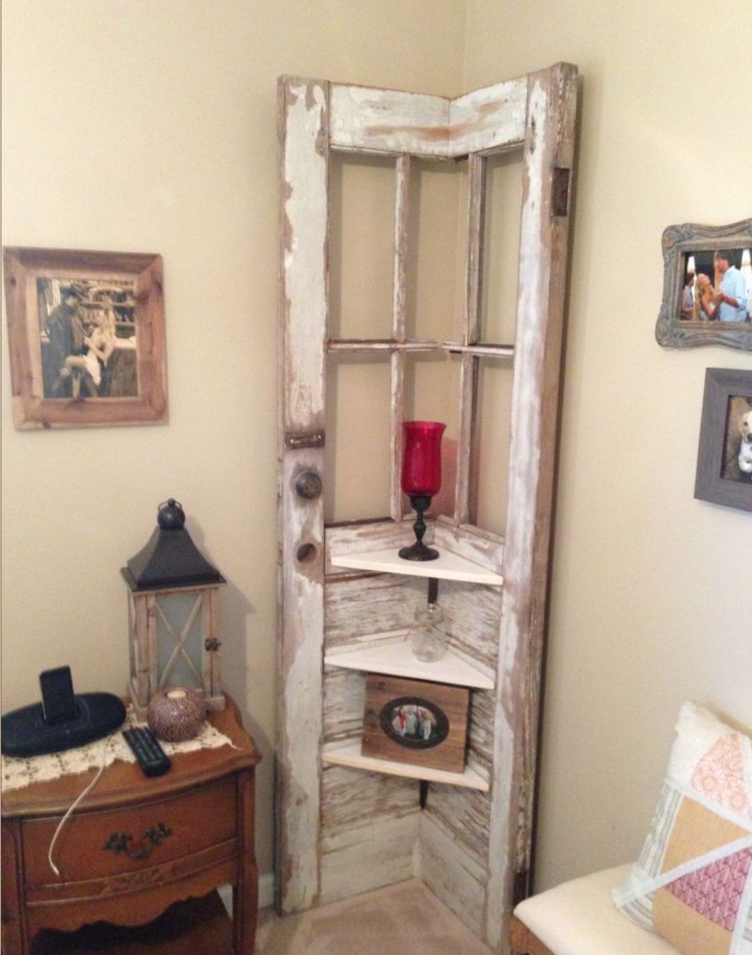 A corner shelf made from an old, distressed white wooden door frame, holding a red glass vase and small framed photos