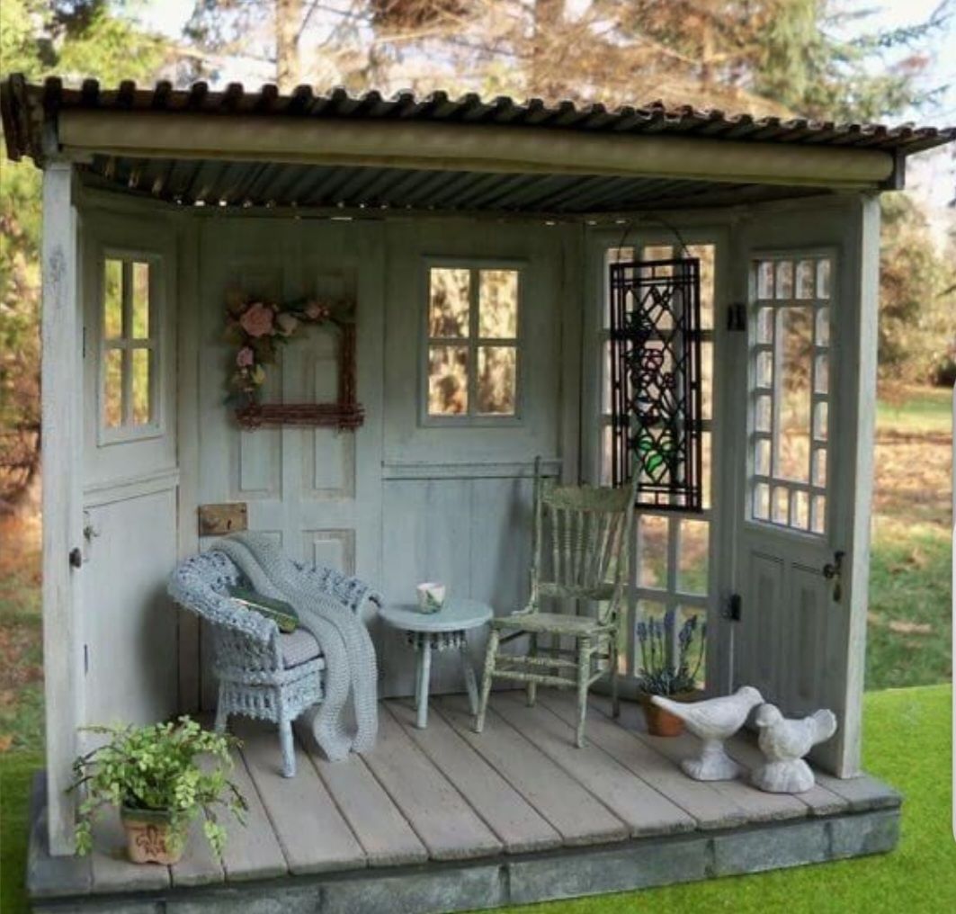 A small, rustic outdoor seating area made of repurposed doors, featuring a wicker chair, wooden chair, table, and decor