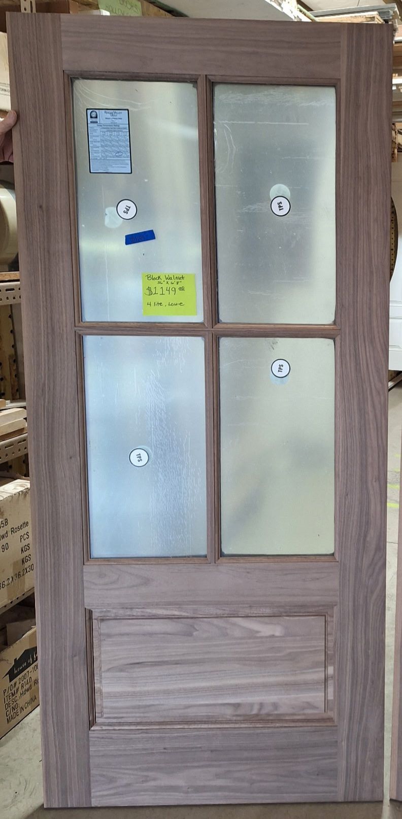 A wooden door with four glass panels above a single rectangular wood panel, standing in a warehouse setting.