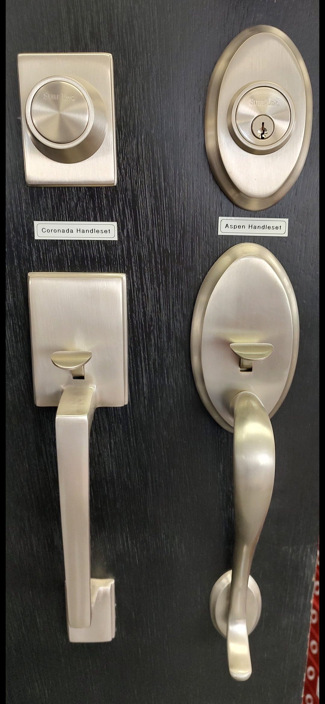Two brushed-nickel door hardware sets with deadbolts and matching vertical handles mounted on a dark textured board.