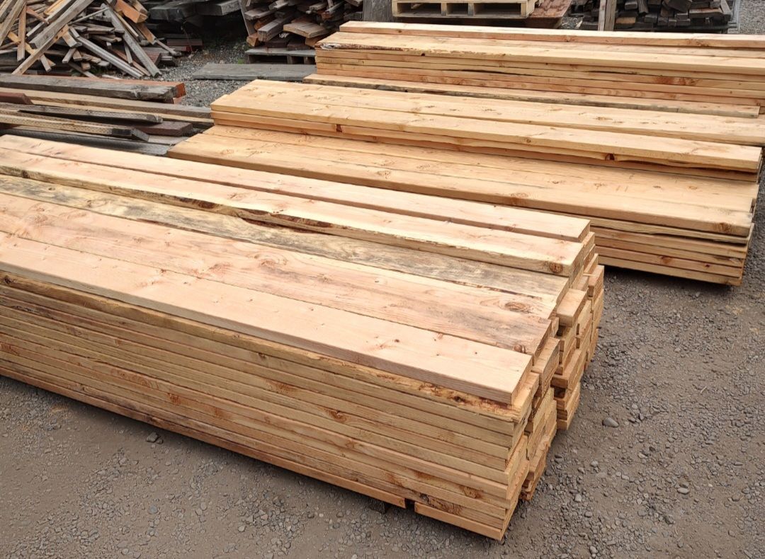 Two stacks of rough-cut light-colored wooden planks arranged on gravel outdoors