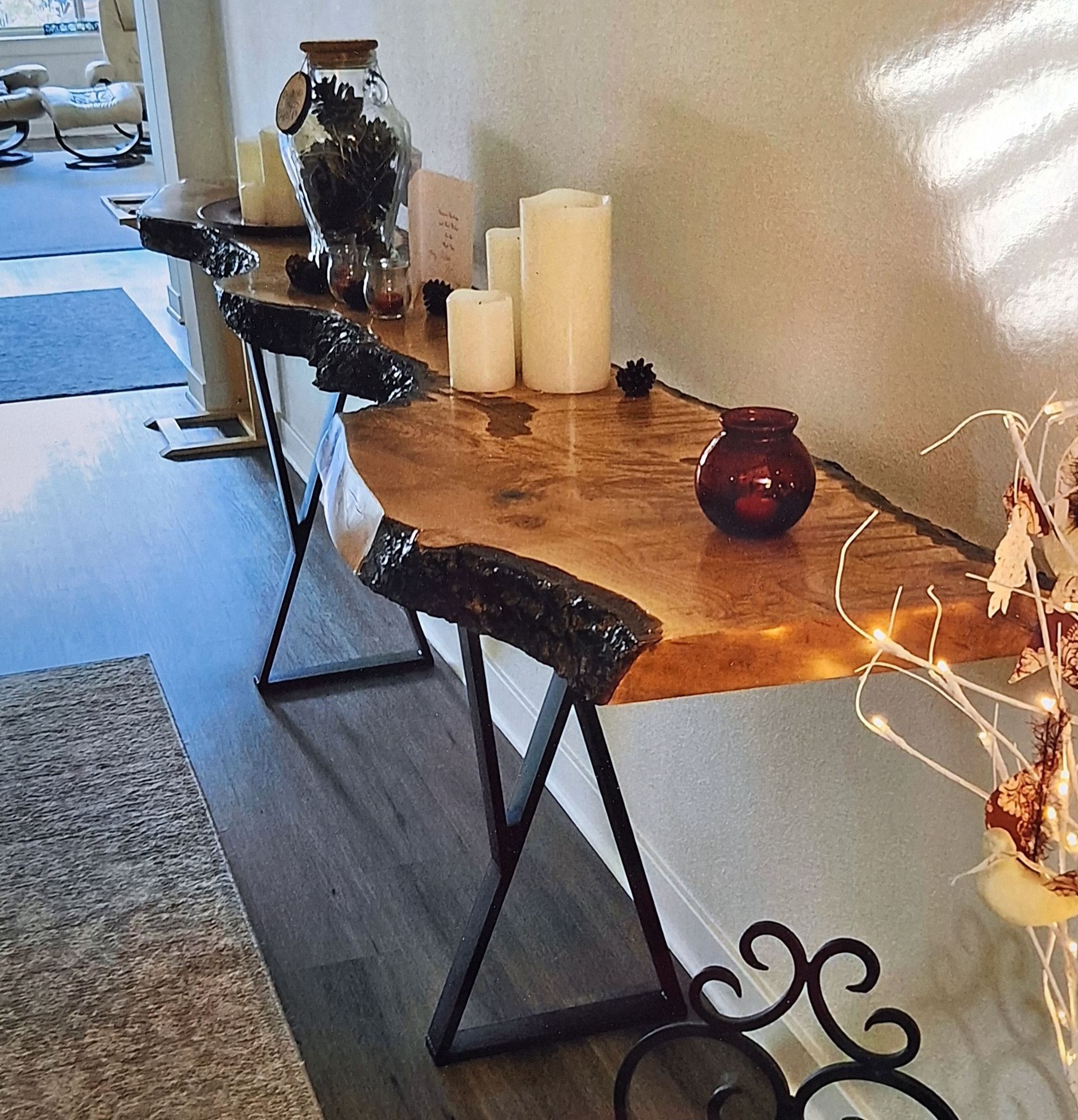 A long, live-edge wood console table with black geometric metal legs sits against a light wall in a hallway