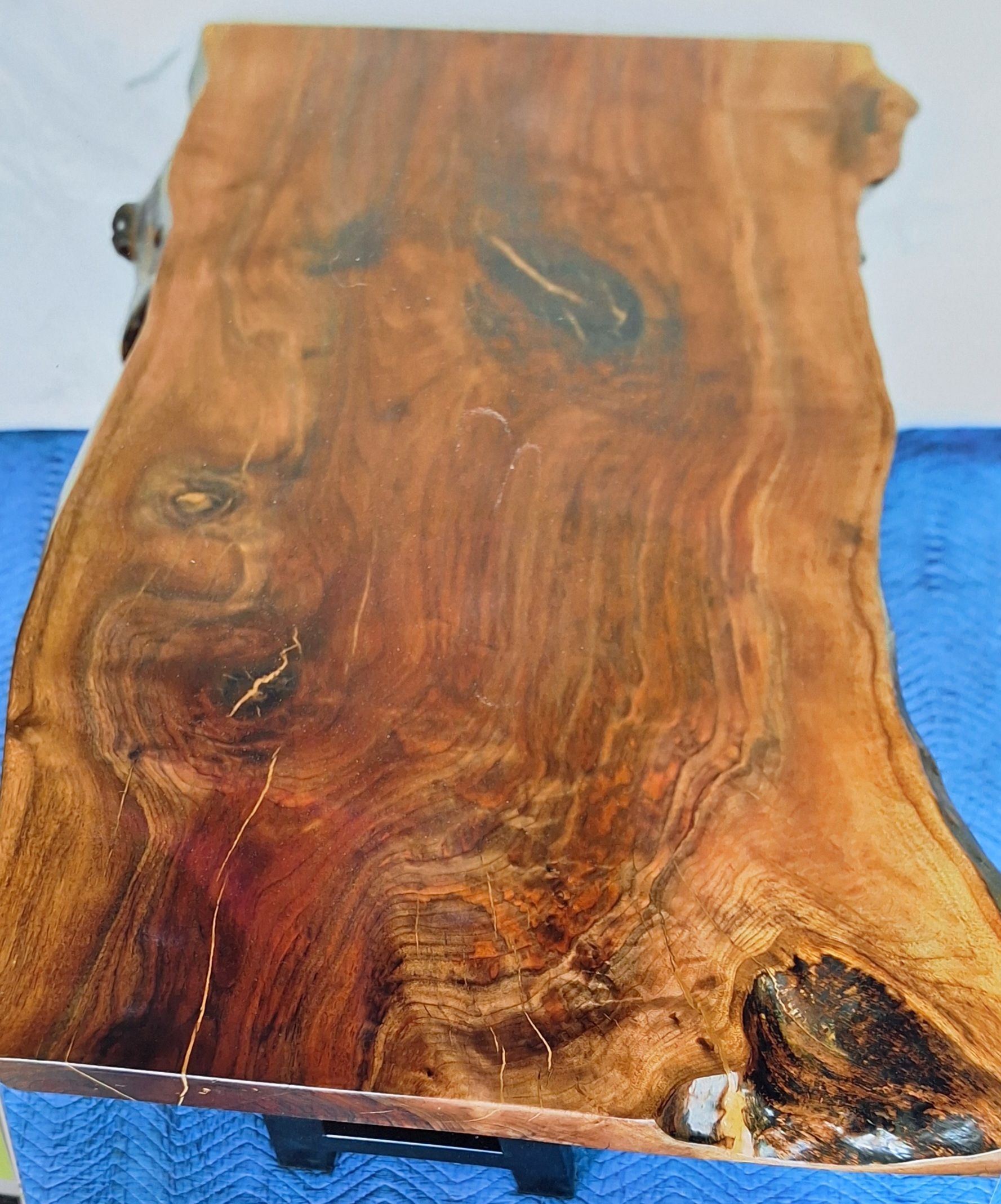 A close-up of a rustic, live-edge wood slab with rich brown tones, visible grain patterns, natural knots, and resin fills