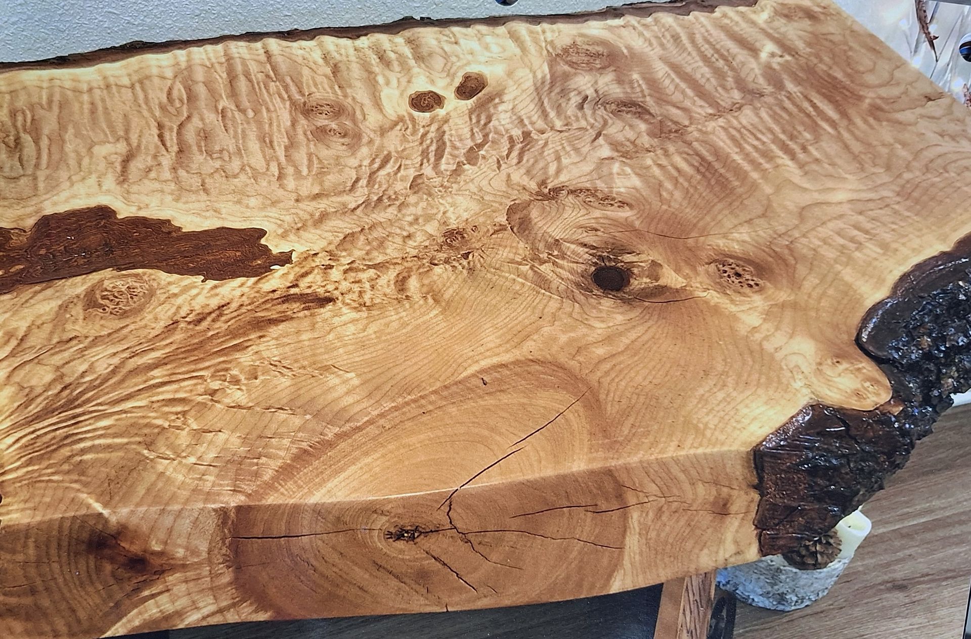 A natural-edge wood slab tabletop with a prominent swirling grain pattern, knots, and bark detailing on the side