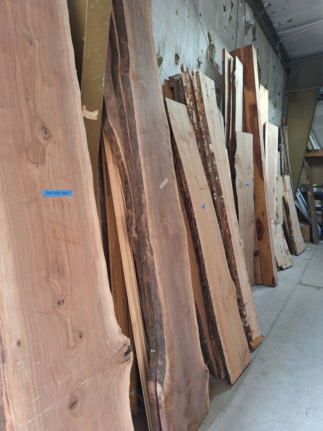 A row of large, unedged wooden slabs with natural bark edges leaning against a wall in a workshop