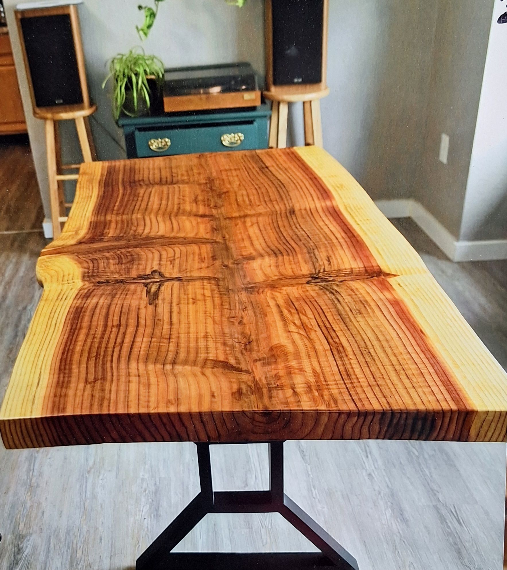 A live-edge wood table with a rich, orange-brown grain and light-colored edges, supported by a black metal base