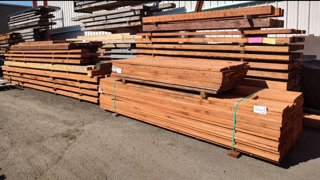 Stacked wooden lumber beams and planks outdoors on an asphalt yard